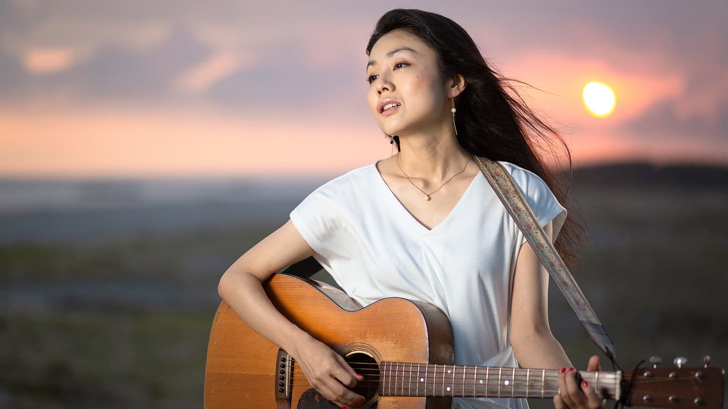 夕日を背景にギターを弾く女性